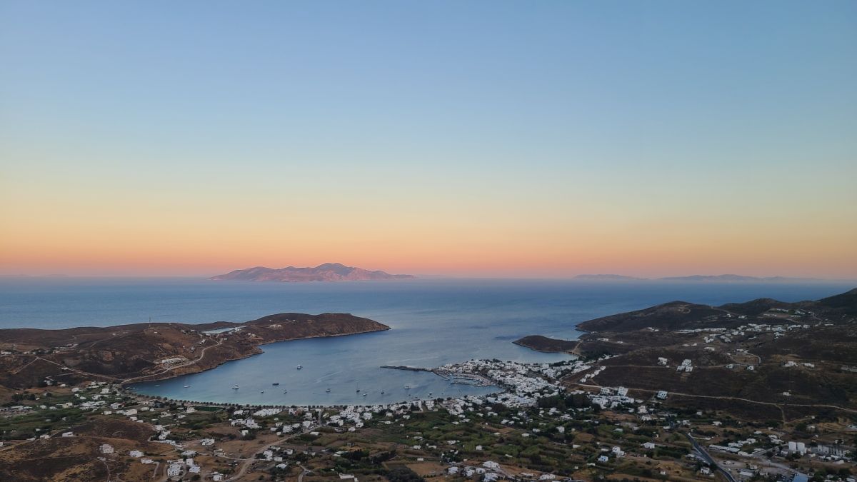 Sunset over a bay and village on a Greek island, with another island on the horizon